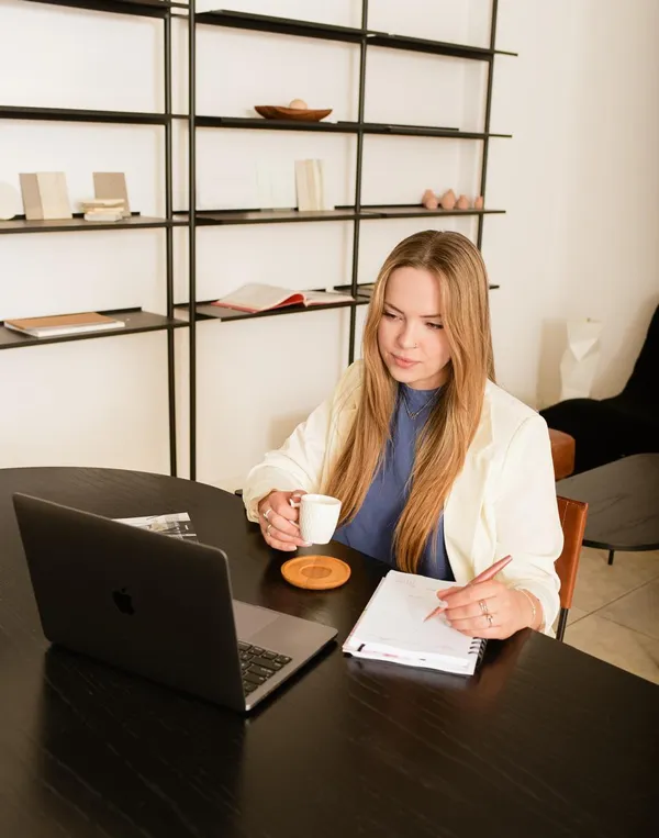 Mariana Marchetti à mesa com uma xícara de café, anotando em um caderno